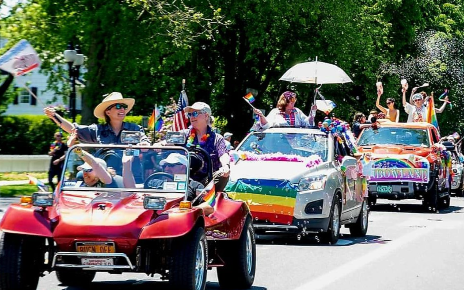 photo of a parade of cars decorated for the pride parade, occupants waving flags and smiling